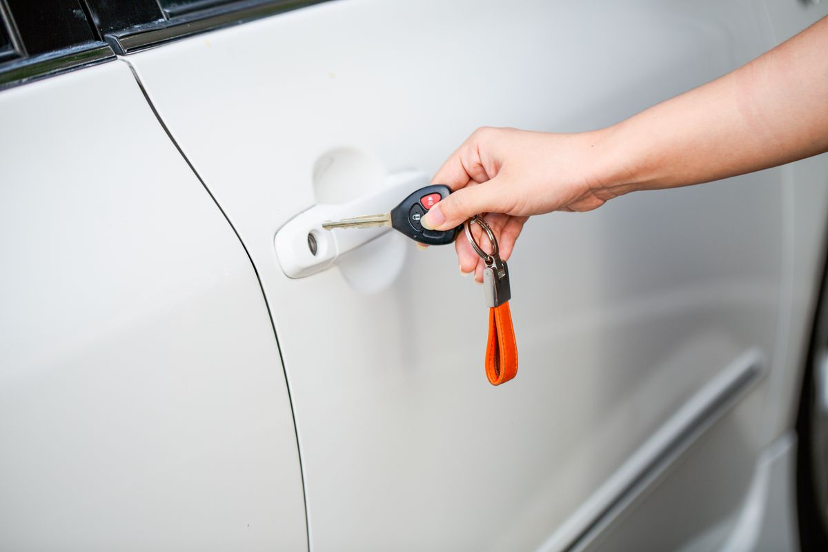 Main tenant une télécommande de clé de voiture près d'une portière