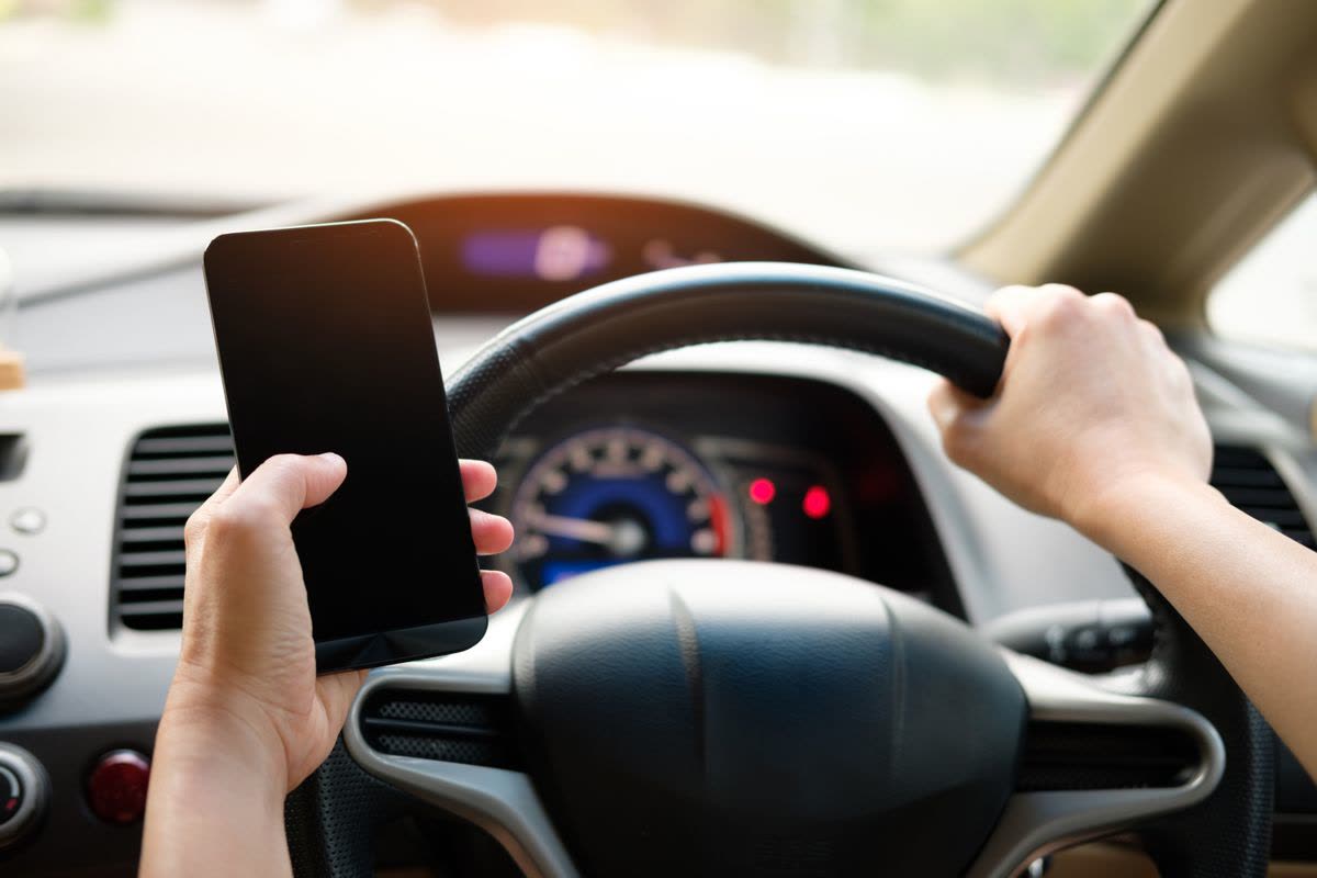 Conducteur tenant un smartphone d'une main et le volant de l'autre